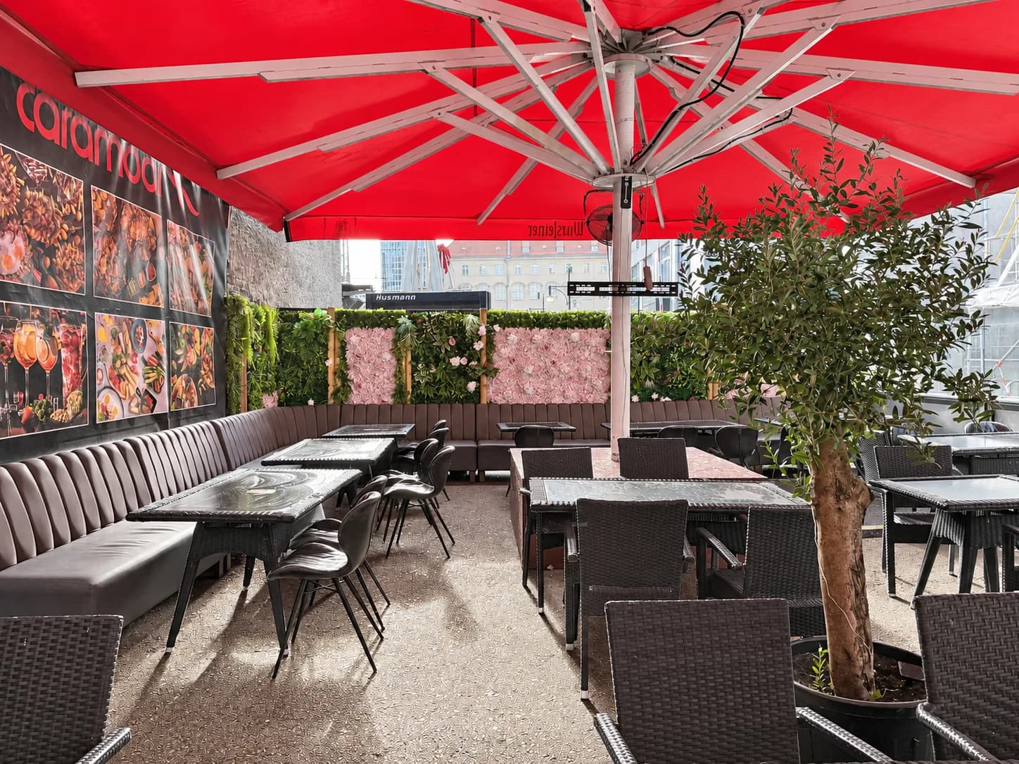 Carambar terrace under a large red parasol with bench seating, tables and an olive tree