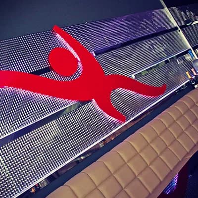 Red Carambar figure in front of the illuminated wall in the club, with the upholstered bench below